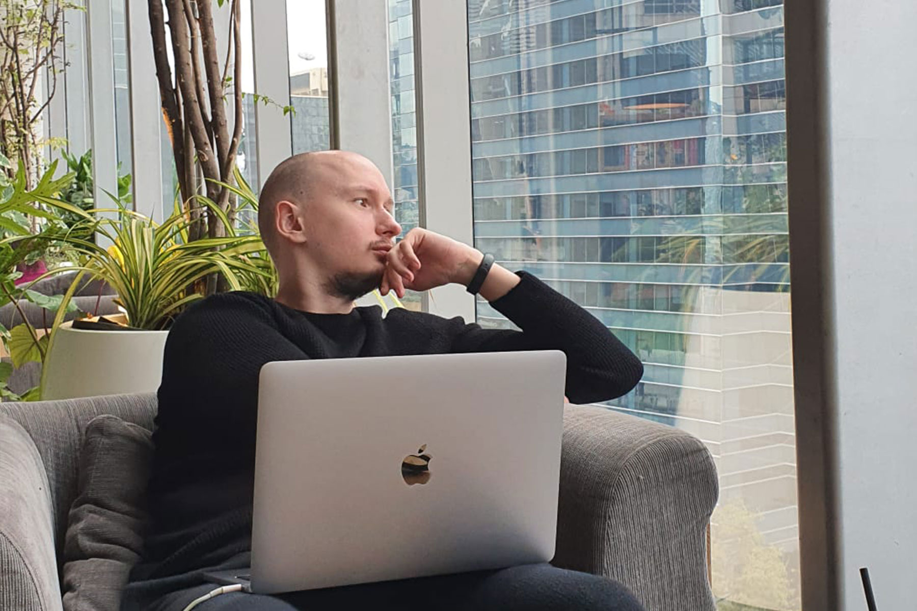 Simon schaut aus dem Fenster mit dem Mac Book auf dem Schoss